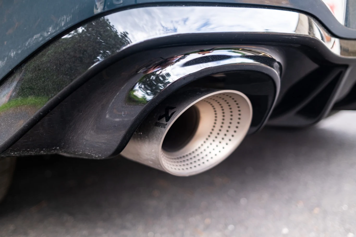 Metaliczna końcówka tłumika samochodowego z perforowanym wnętrzem, otoczona czarnym elementem z tworzywa.