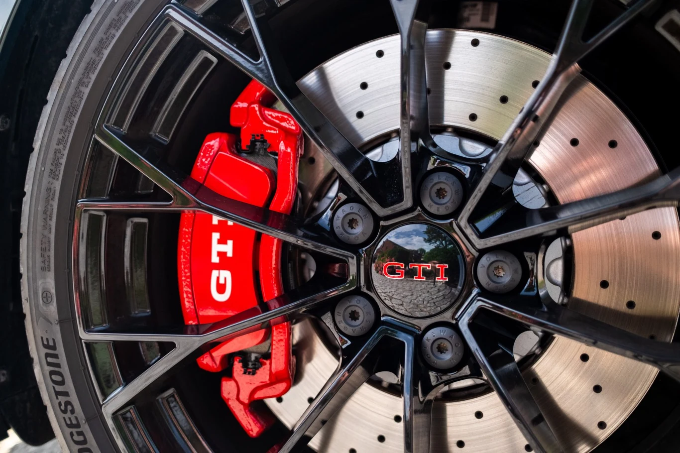 Czarna felga aluminiowa z czerwonym zaciskiem hamulcowym GTI oraz perforowaną tarczą hamulcową.