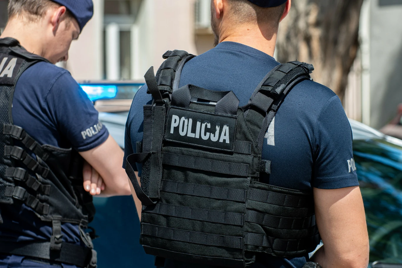 Zdj. ilustracyjne. Policjanci zatrzymali kobietę, która wszczęła awantur w przychodni w Ełku Dwóch policjantów w kamizelkach z napisem 'Policja' stoi przy radiowozie przed przychodnią w Ełku.