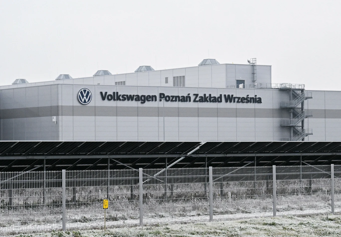 Zwolnienia w koncernie Volkswagen nie powinny dotknąć polskiej załogi (zdj. ilustracyjne) Fabryka Volkswagen Poznań Zakład Września z logo, ogrodzeniem i panelami fotowoltaicznymi na pierwszym planie.