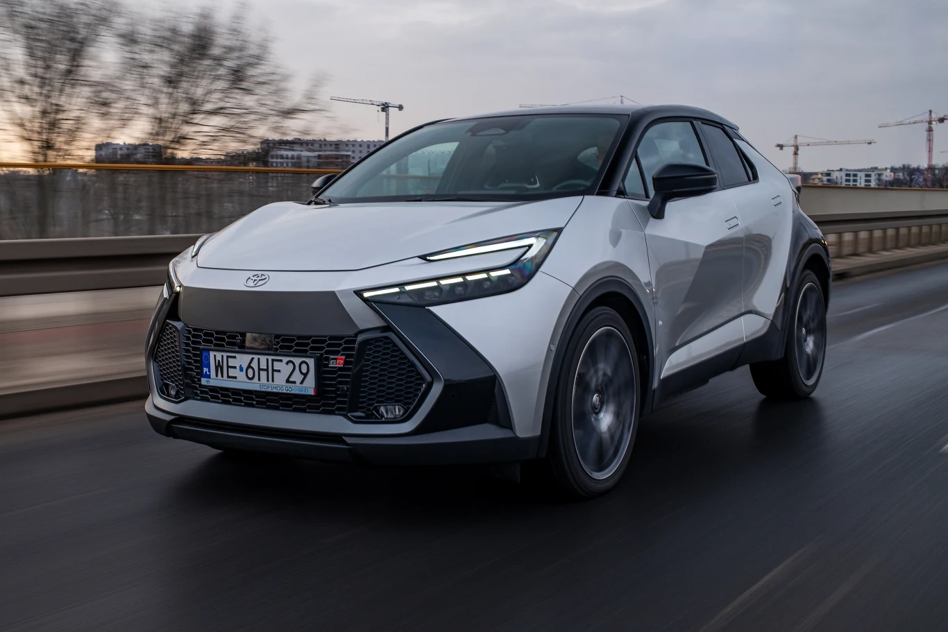 Toyota C-HR kończy 10 lat. Toyota C-HR, biało-czarny SUV z LED-owymi reflektorami, na miejskiej drodze przy pochmurnym niebie.