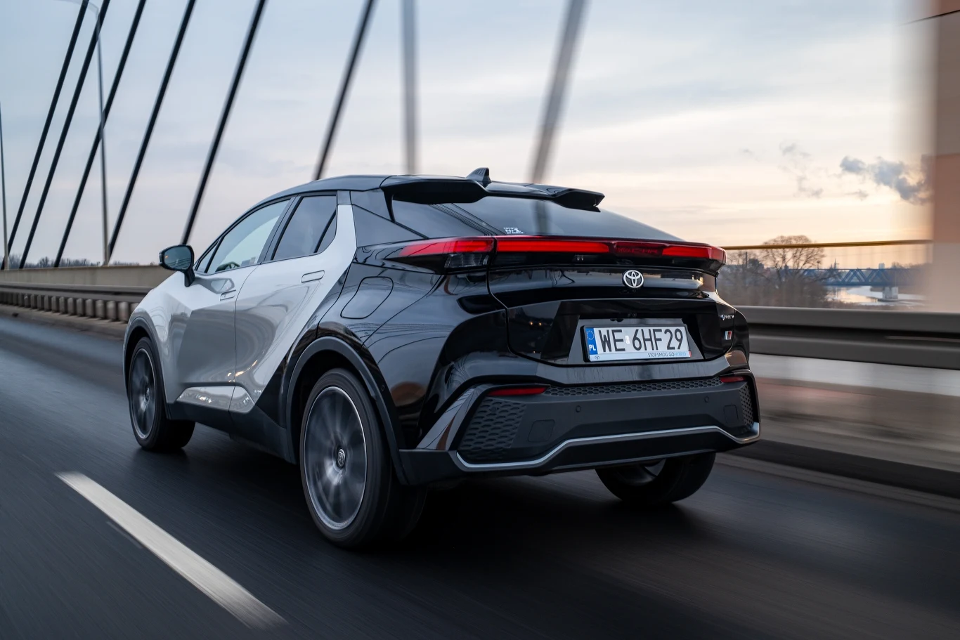 Nowoczesny, czarny SUV marki Toyota przejeżdżający przez most, dynamiczna sylwetka pojazdu podkreślona przez wyraziste linie nadwozia oraz unikalny kształt tylnych świateł LED.