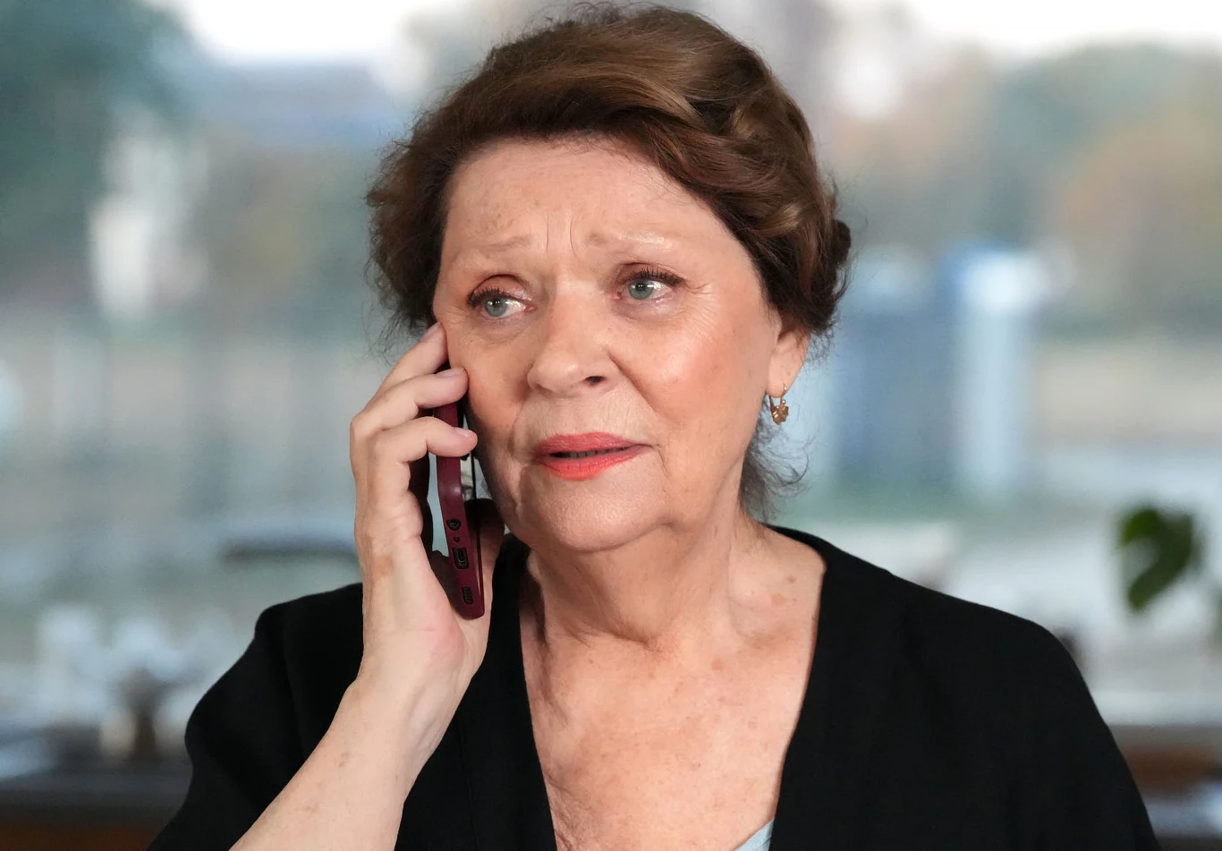 "Barwy szczęścia" Starsza kobieta w czarnym swetrze, z zaniepokojoną miną, rozmawia przez telefon komórkowy.