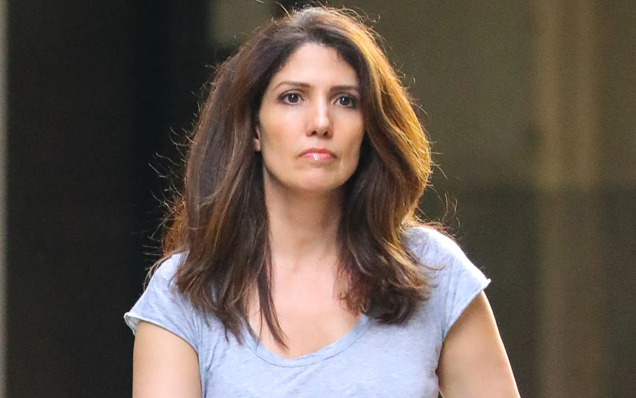 Lynda Lopez jest bardzo podobna do Jennifer Kobieta z długimi, rozpuszczonymi włosami, ubrana w jasnoszarą koszulkę z krótkim rękawem, stoi na neutralnym tle.