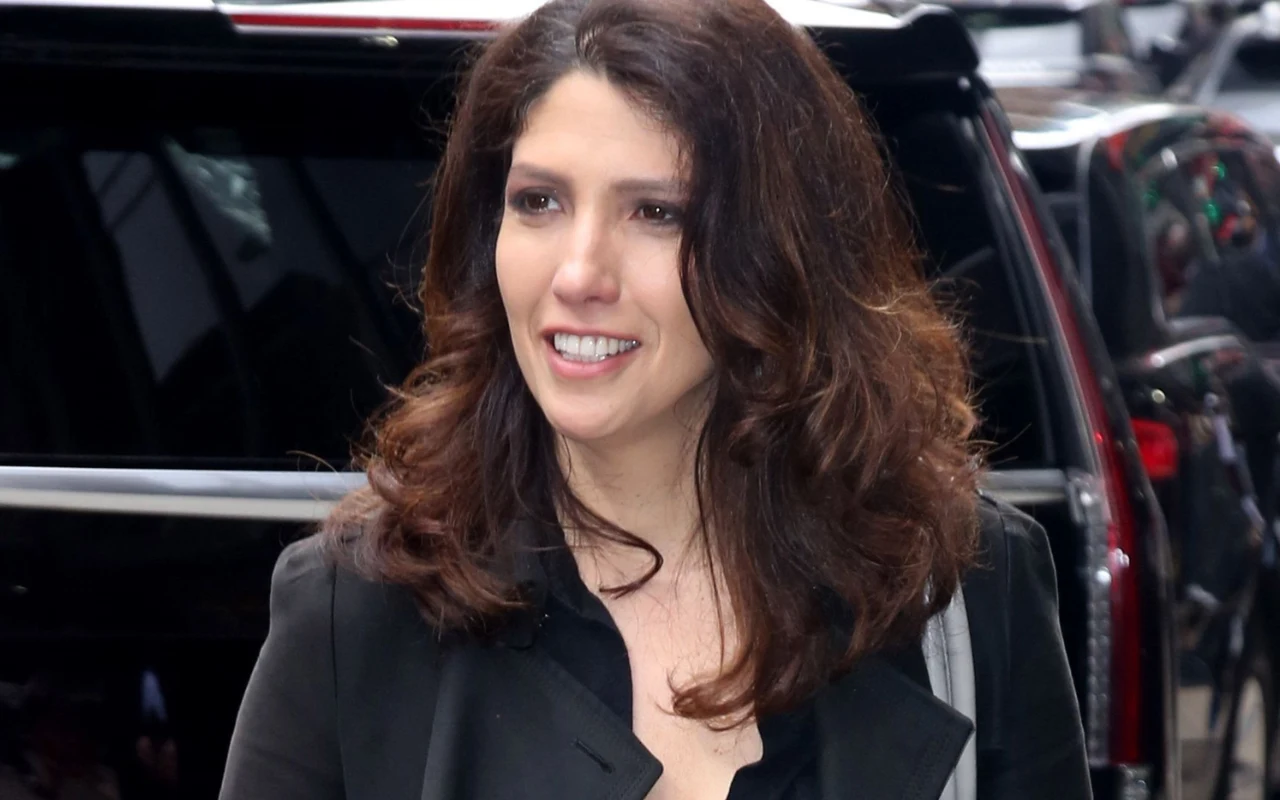 Lynda Lopez urodziła się w 1971 roku, czyli jest od Jennifer młodsza o niespełna dwa lata. Uśmiechnięta kobieta o ciemnych, falowanych włosach ubrana w czarną marynarkę stoi na tle czarnego samochodu.