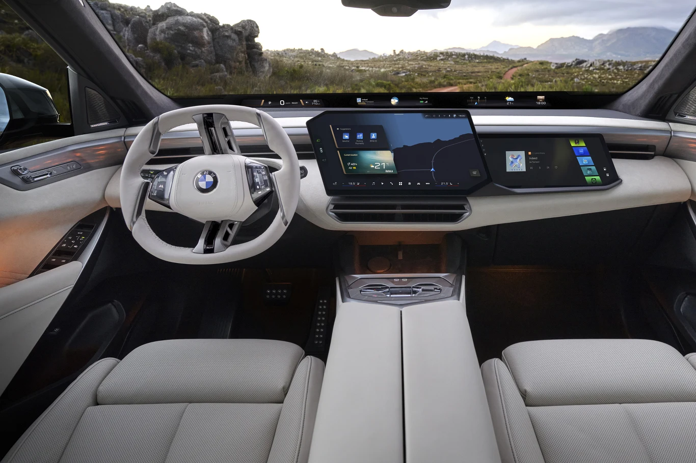 Luksusowe, jasne wnętrze samochodu marki BMW z dwoma dużymi ekranami na desce rozdzielczej, nowoczesną kierownicą o nietypowym kształcie oraz eleganckimi fotelami pokrytymi skórą.