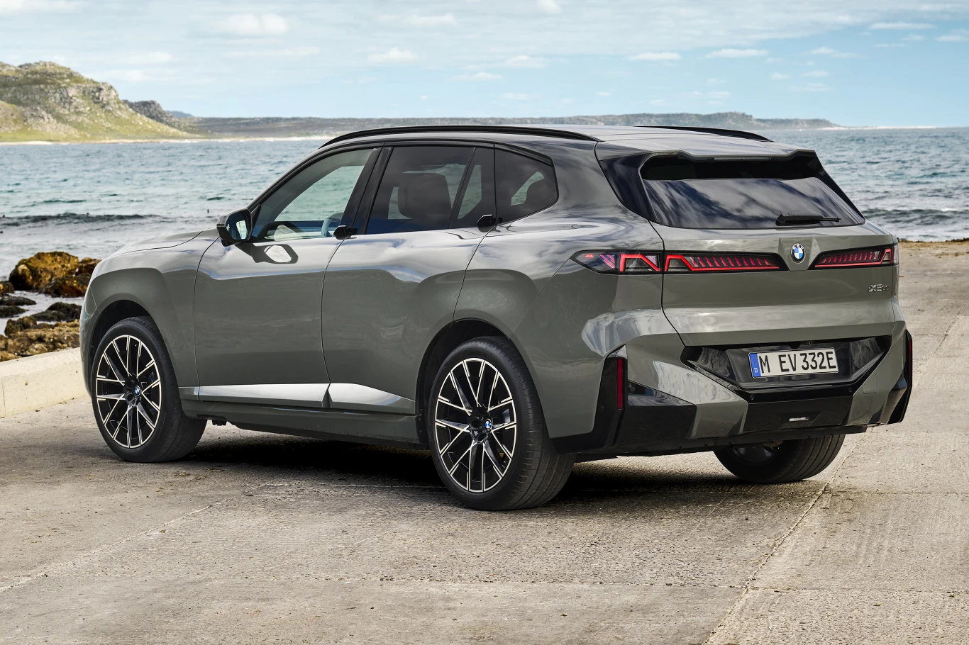 Nowoczesny, szary SUV marki BMW zaparkowany nad brzegiem morza, z charakterystycznymi tylnymi lampami LED i dynamiczną sylwetką.