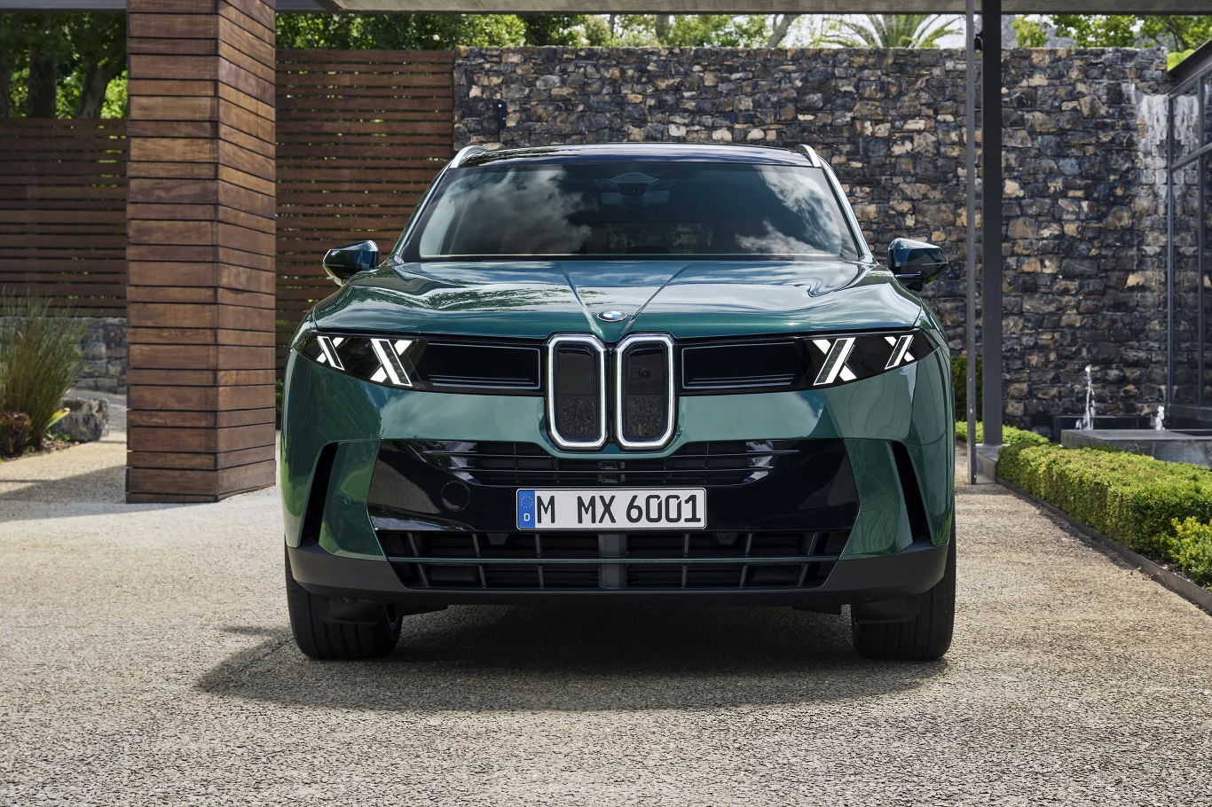 Luksusowy, zielony SUV BMW z nowoczesnymi reflektorami LED i charakterystycznym dużym grillem, zaparkowany przodem do widza na tle nowoczesnej architektury oraz minimalistycznego ogrodu.