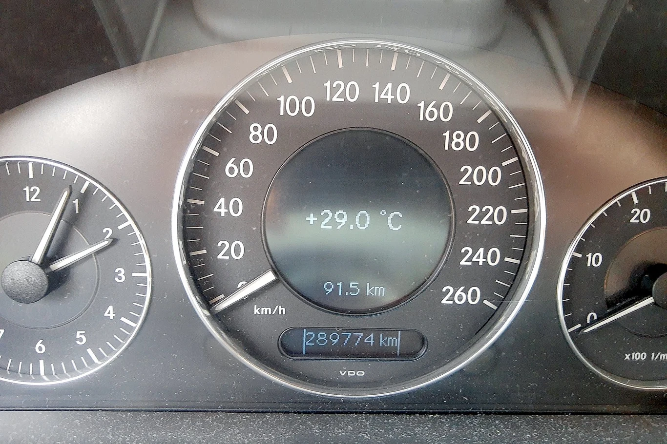 Zbliżenie na wskaźniki deski rozdzielczej samochodu z czytelnym licznikiem kilometrów, temperaturą zewnętrzną 29°C, wskazaniem 91,5 przejechanych kilometrów oraz aktualnym przebiegiem 289774 km.