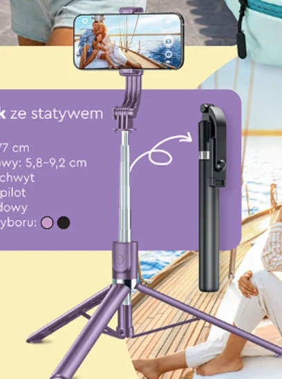 Selfie stick w kolorze fioletowym z zamontowanym smartfonem ustawionym poziomo oraz osobnym pilotem, całość rozłożona w trybie statywu na drewnianym pokładzie łodzi.