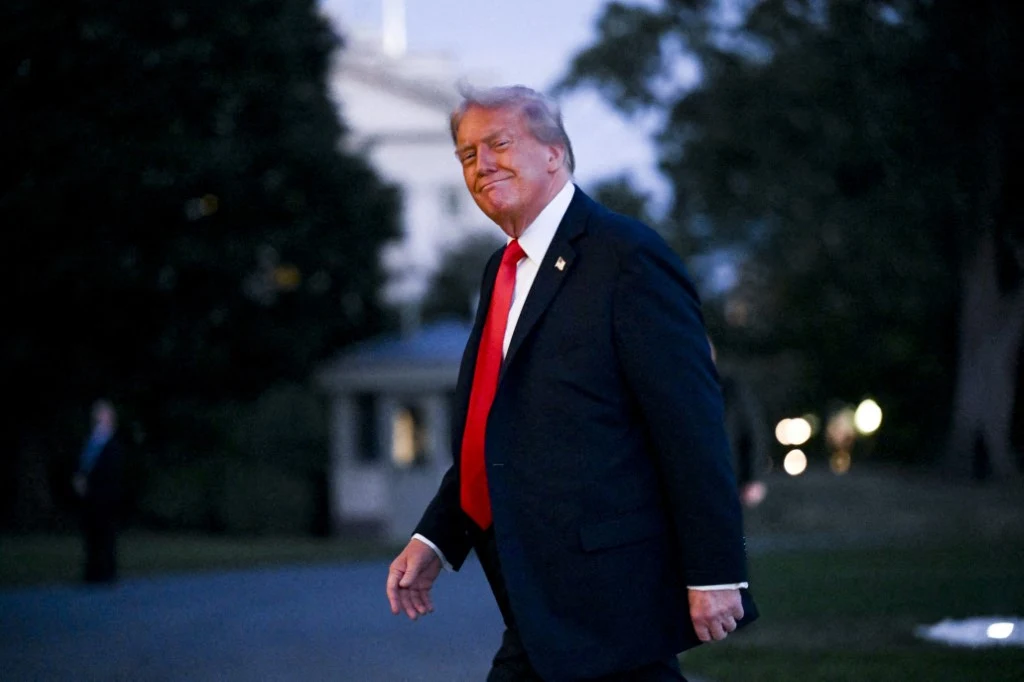 Donald Trump cieszy się z poszerzenia swojej władzy przez amerykański Sąd Najwyższy Donald Trump w ciemnym garniturze i czerwonym krawacie idzie na zewnątrz o zmierzchu, w tle światła i drzewa.