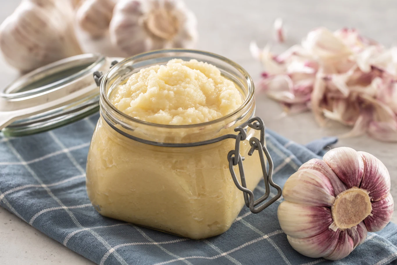 podstawowym składnikiem skordalii jest czosnek Słoik z kremowym puree czosnkowym ustawiony na ściereczce obok główki czosnku oraz obranych ząbków.