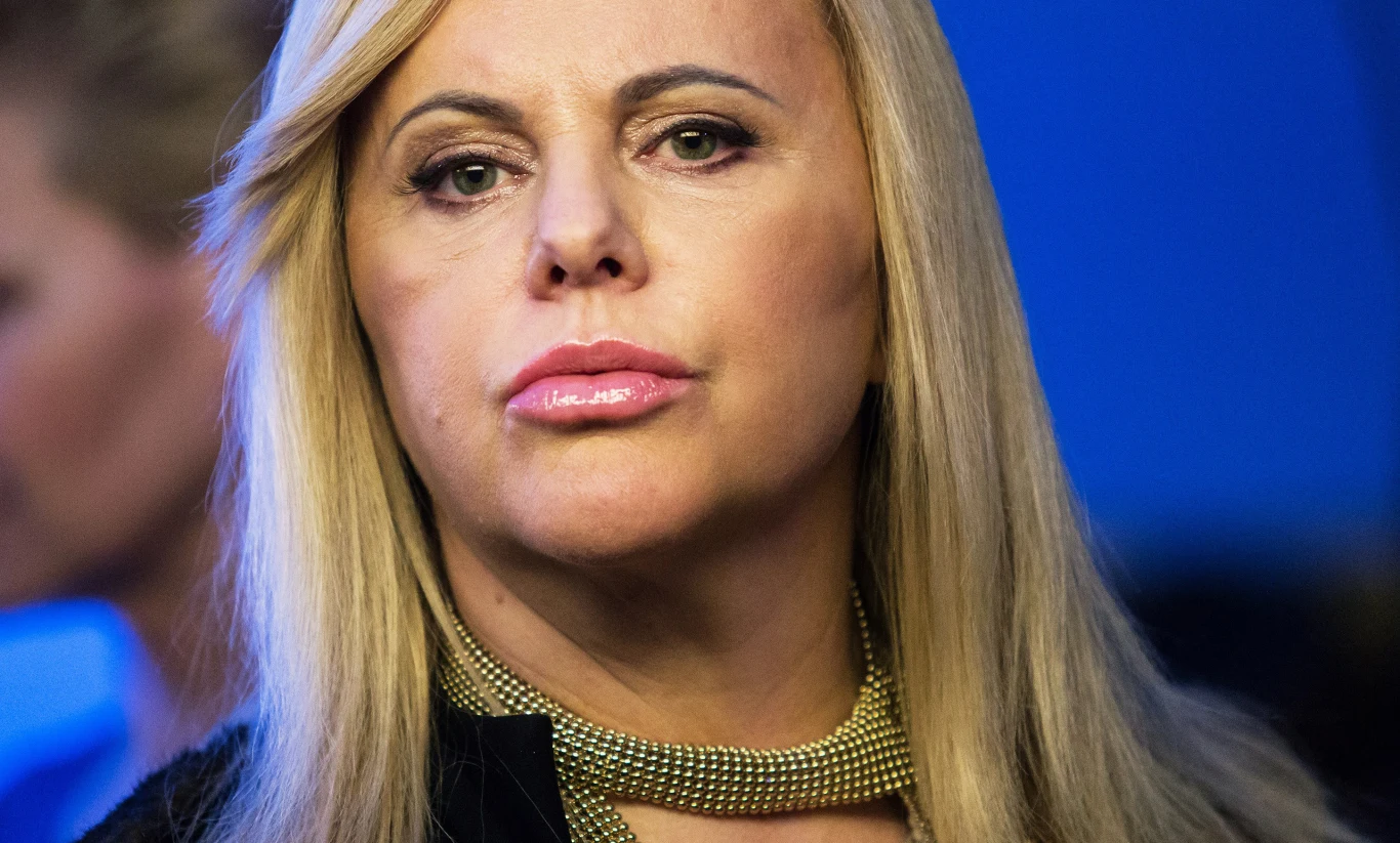 Joanna Kurowska Joanna Kurowska z długimi blond włosami w czarnej odzieży i złotym naszyjniku na niebieskim tle.