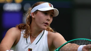 Tenisistka w białym stroju sportowym i czapce z daszkiem, trzymająca zieloną rakietę podczas meczu.