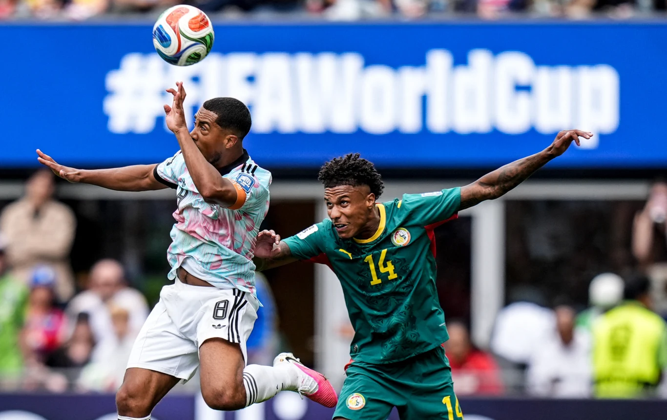 Mecz Belgia - Senegal na mundialu 2026 Dwóch piłkarzy rywalizuje o piłkę w powietrzu podczas meczu, jeden w jasnej koszulce, drugi w zielonym stroju z numerem 14, na tle widocznego hasła FIFA World Cup.