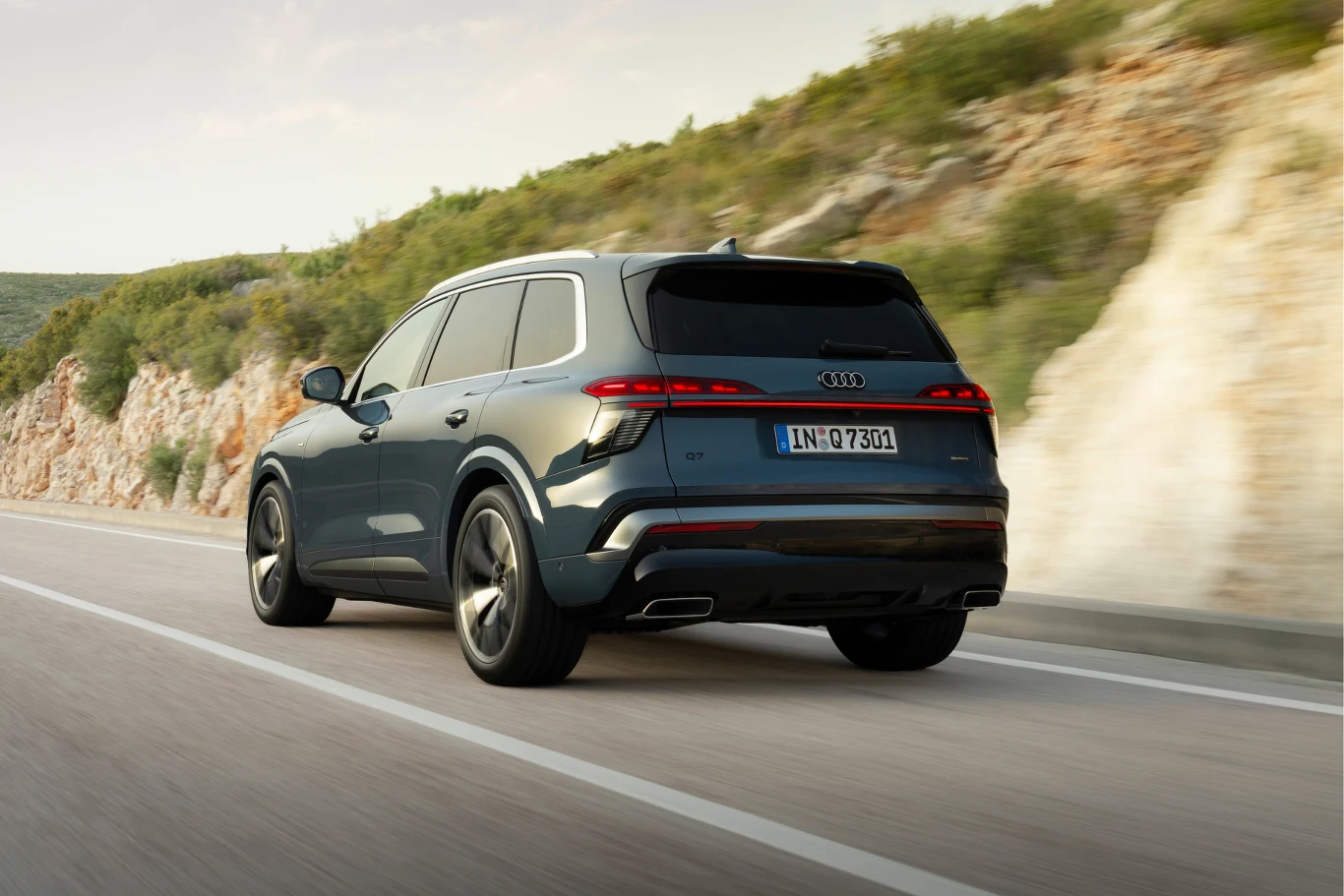 Nowoczesny SUV Audi w ciemnym kolorze poruszający się po górskiej, asfaltowej drodze, w otoczeniu skalistych zboczy porośniętych niską roślinnością.