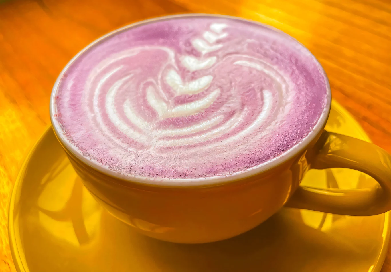 Koreanki uważają goguma latte za eliksir piękna. Piją regularnie, by poprawić stan skóry. Filiżanka goguma latte o różowym kolorze na żółtym spodku, z wzorem z mlecznej pianki na wierzchu.