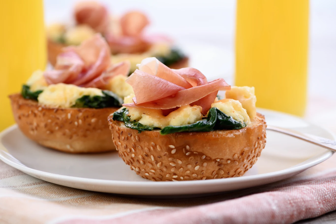 Pyszna kanapki z jajkiem i szynką parmeńską w wersji na ciepło Połówka bułki z sezamem, jajecznicą, szpinakiem i szynką parmeńską podana na ciepło.