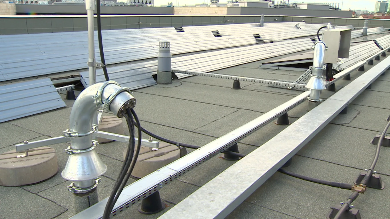 Na dachu uczelni uszczelnione są nawet kable Elementy instalacji fotowoltaicznej na dachu budynku, metalowe konstrukcje wsporcze, kable oraz fragmenty paneli słonecznych ułożonych w rzędach.