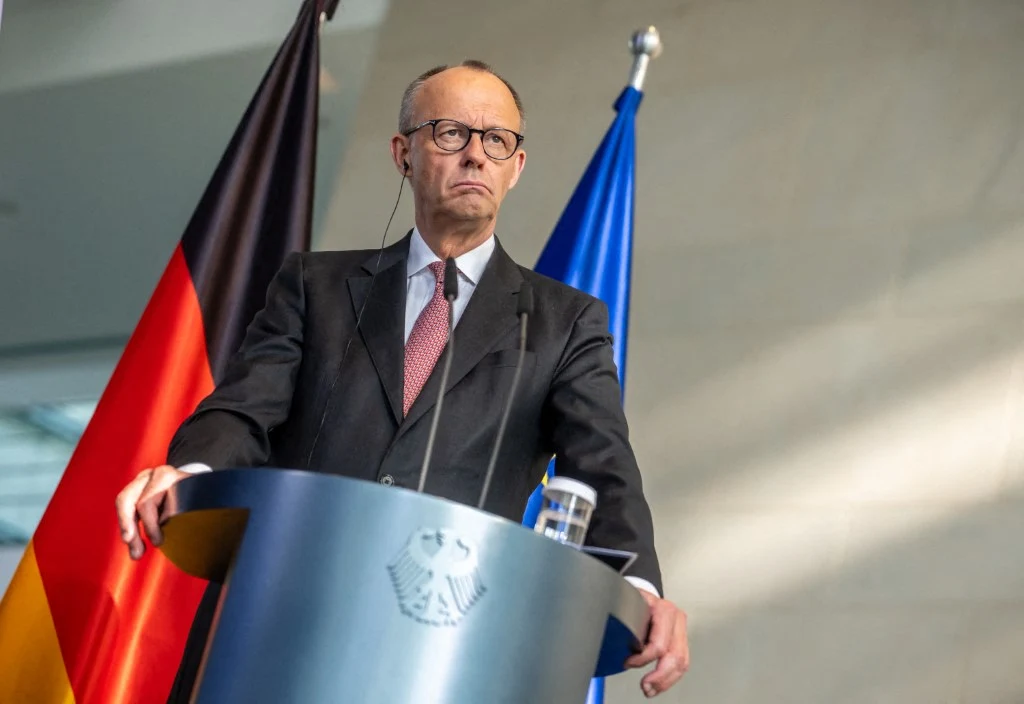 Propozycja reformy gospodarczej Friedricha Merza spotkała się z mieszanym odbiorem społecznym Friedrich Merz stoi za mównicą z godłem orła, w tle widoczne flagi Niemiec i Unii Europejskiej.