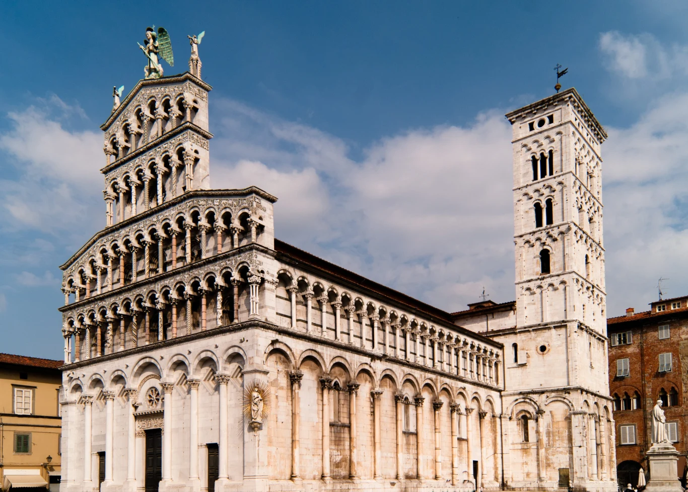 Monumentalna romańska katedra z bogato zdobioną fasadą, trzema kondygnacjami arkad i wysoką dzwonnicą dominującą nad placem.