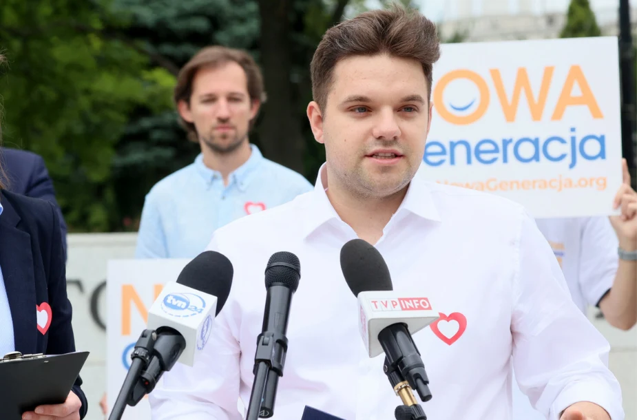 Dawid Kacprzyk Dawid Kacprzyk przemawia do mikrofonów, w białej koszuli z przypiętym serduszkiem, podczas wydarzenia Nowa Generacja.