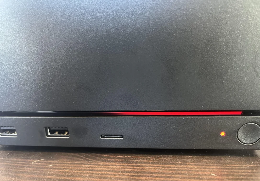 Dolna część czarnego laptopa z widoczną czerwoną linią pod ekranem, dwoma portami USB, czytnikiem kart pamięci oraz świecącą diodą zasilania obok przycisku włącznika.