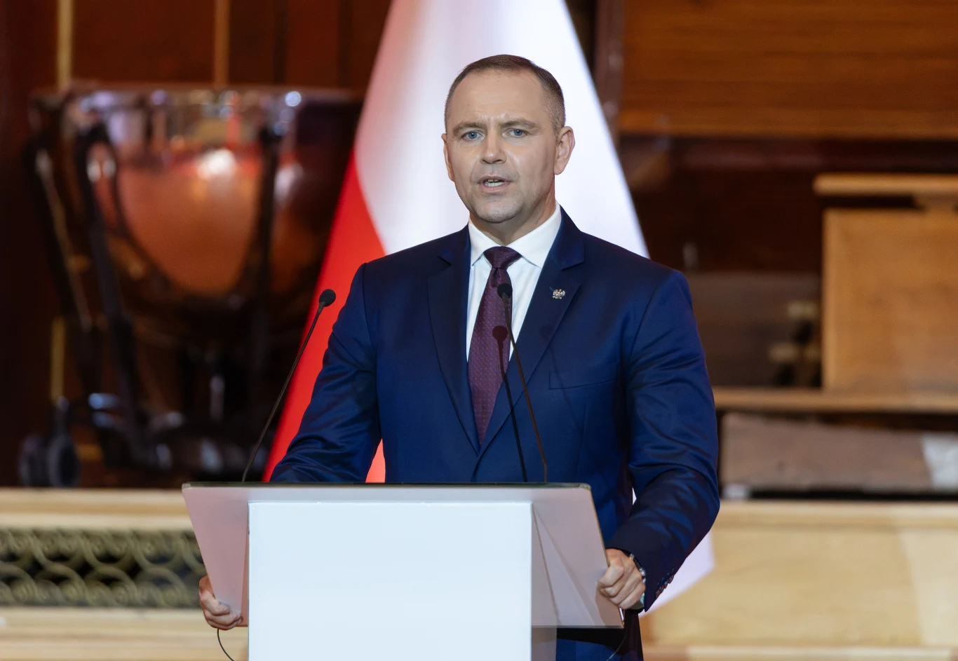 Sędzia TK napisał list do Karola Nawrockiego Prezydent Karol Nawrocki w granatowym garniturze stoi za mównicą z mikrofonami, w tle flaga biało-czerwona.