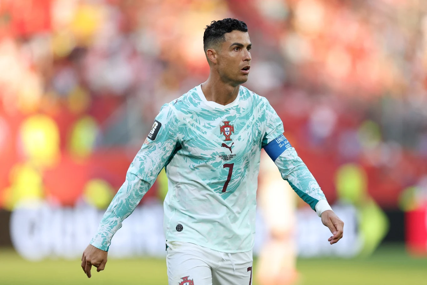 Portugalski piłkarz w jasnej koszulce z numerem 7 i opaską kapitana podczas meczu, skupiony na grze, z dynamicznym tłem stadionu w żywych kolorach.