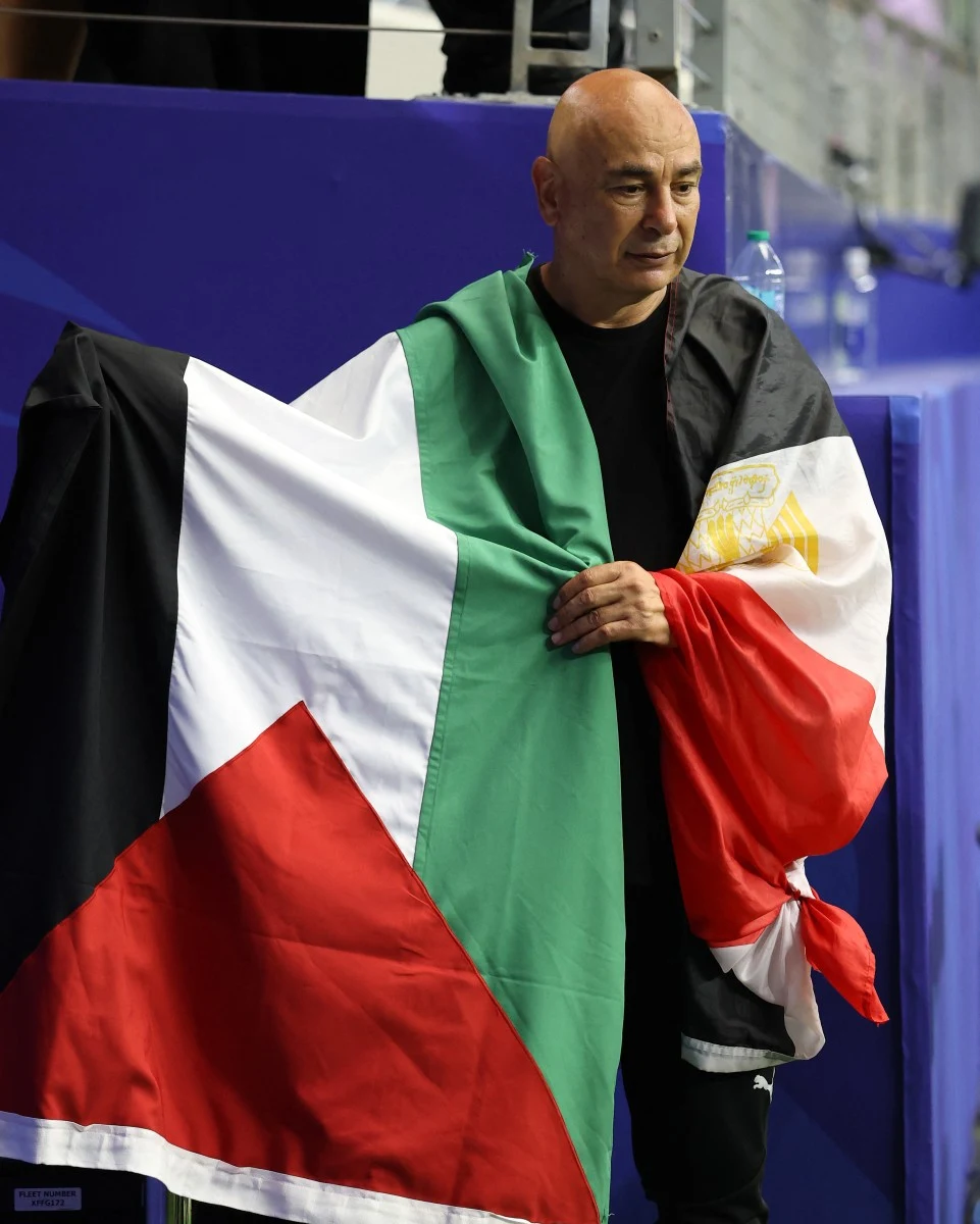 Mężczyzna owinięty flagą Palestyny i Egiptu stojący przy niebieskiej barierce.