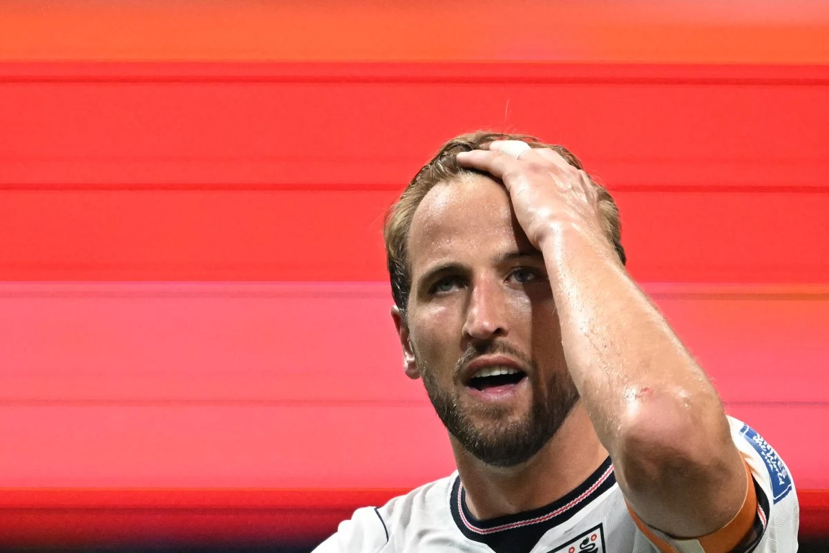 Harry Kane poprowadził Anglię do awansu do 1/8 finału MŚ Piłkarz w białej koszulce z opaską kapitana na ramieniu, z wyrazem zmęczenia lub rozczarowania, trzyma się za głowę na tle czerwonych, rozmytych pasów.