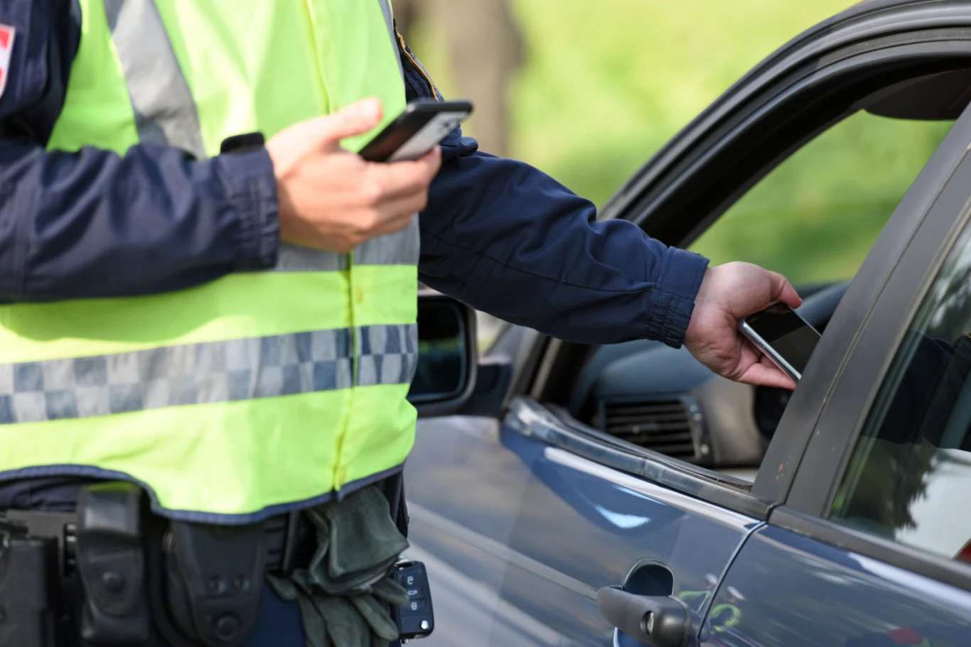 Wiele mandatów, jakie można dostać za granicą, jest zaskakujących dla polskich kierowców Policjant w odblaskowej kamizelce sprawdza wypisuje mandat przy otwartym oknie samochodu osobowego.