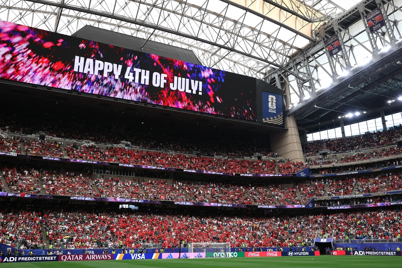 Tłum kibiców na stadionie pod ogromnym ekranem z napisem „HAPPY 4TH OF JULY!” podczas sportowego wydarzenia.
