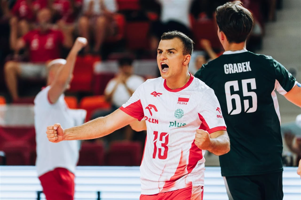 Zawodnik polskiej reprezentacji siatkówki w białoczerwonym stroju, zaciśnięte pięści i okrzyk radości, obok niego inny siatkarz w ciemnozielonej koszulce z napisem Grabek i numerem 65.