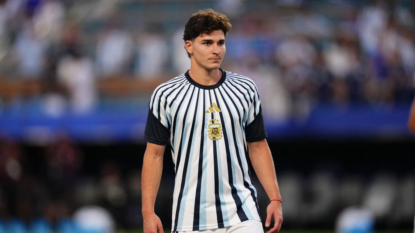 Julian Alvarez Piłkarz w biało-niebieskiej koszulce z herbem Argentyny spaceruje po murawie stadionu.
