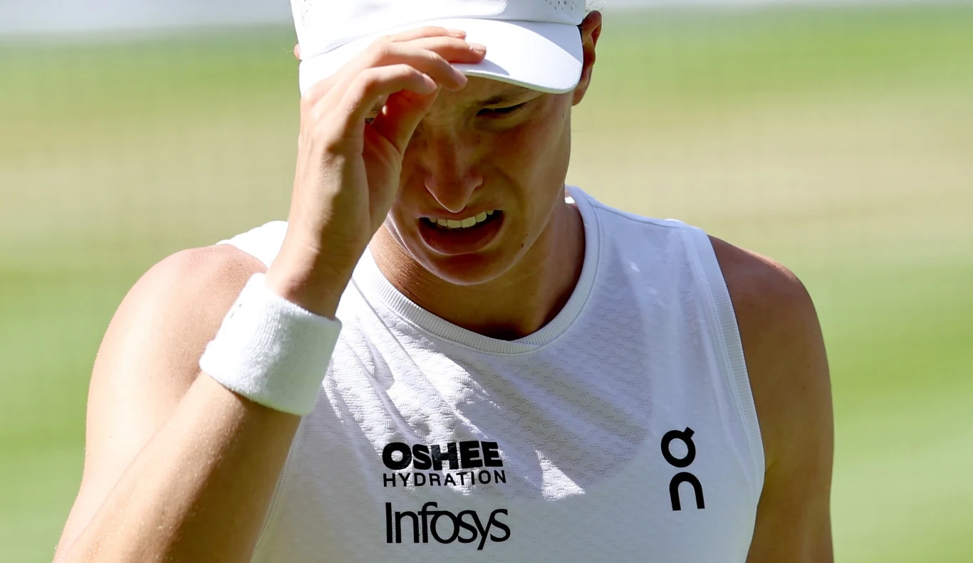 Sportowiec w białej koszulce i czapce z daszkiem poprawia nakrycie głowy, wyraźnie skupiony i skoncentrowany, widoczne logotypy marek Oshee, Infosys i On na ubraniu.