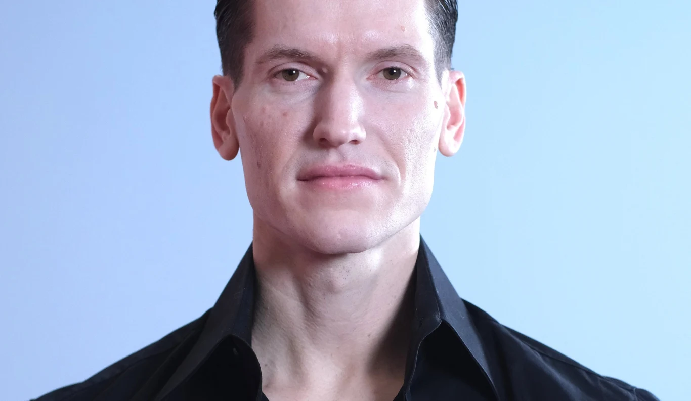Jacek Jeschke Jacek Jeschke w czarnej koszuli pozujący na tle jasnoniebieskiej ściany.