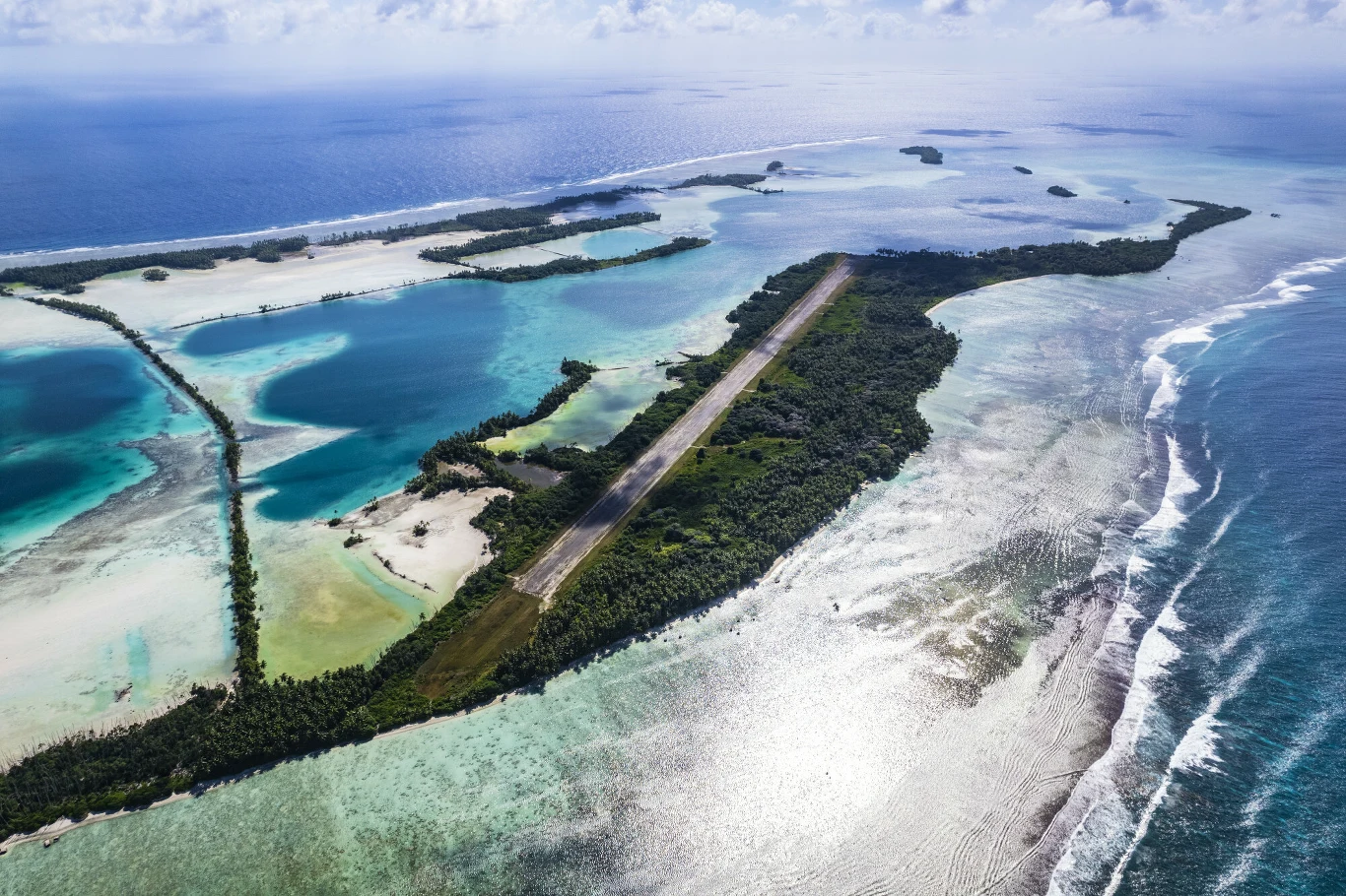 Atol Palmyra Pasy startowe lotniska przebiegające przez tropikalną wyspę otoczoną turkusową wodą, lagunami oraz bujną zielenią, z widocznym oceanem w tle.