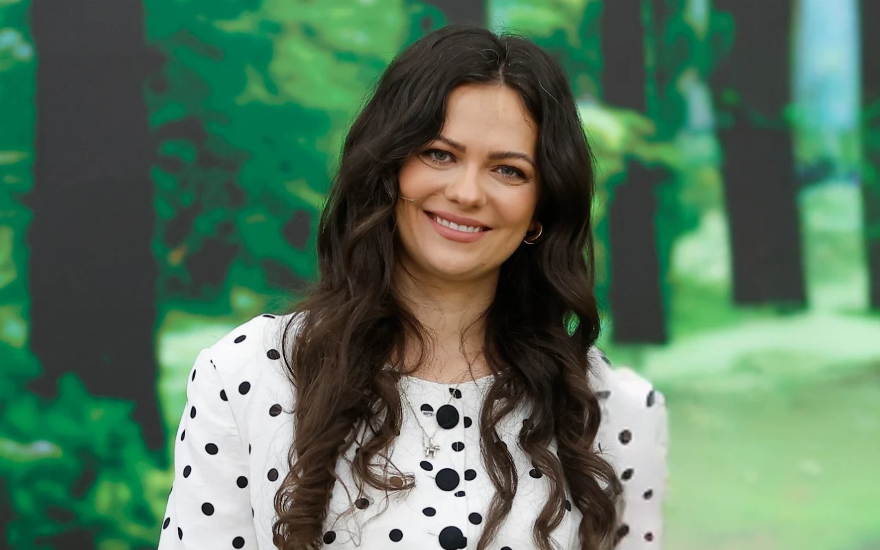 Dietetyczka Paulina Ihnatowicz w "halo tu polsat" Uśmiechnięta kobieta z długimi, ciemnymi włosami w białej bluzce w czarne grochy na tle zielonych drzew.