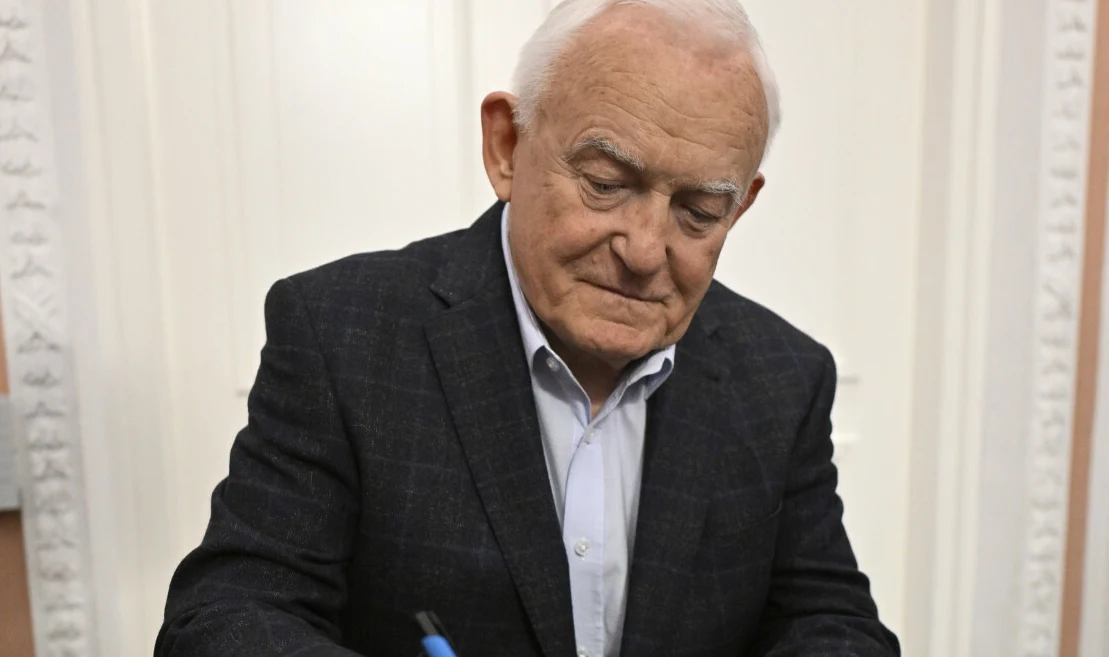 Leszek Miller Leszek Miller z siwymi włosami w ciemnej marynarce podpisuje dokument długopisem, skupiony nad wykonywaną czynnością.