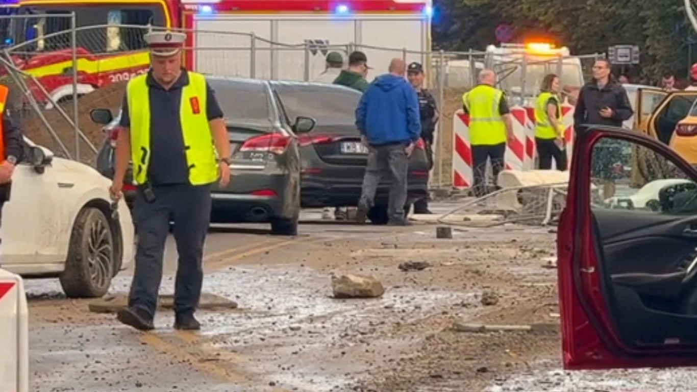 Służby na miejscu wypadku, w tle uszkodzone auta Służby ratunkowe, rozbite samochody i porozrzucane gruzowisko na ulicy po wypadku drogowym, wokół stoją funkcjonariusze i cywile.