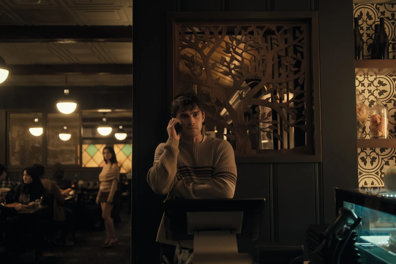 Kadr z filmu "Obsesja" / UIP Mężczyzna w jasnym swetrze rozmawia przez telefon przy stanowisku obsługi w lokalu.