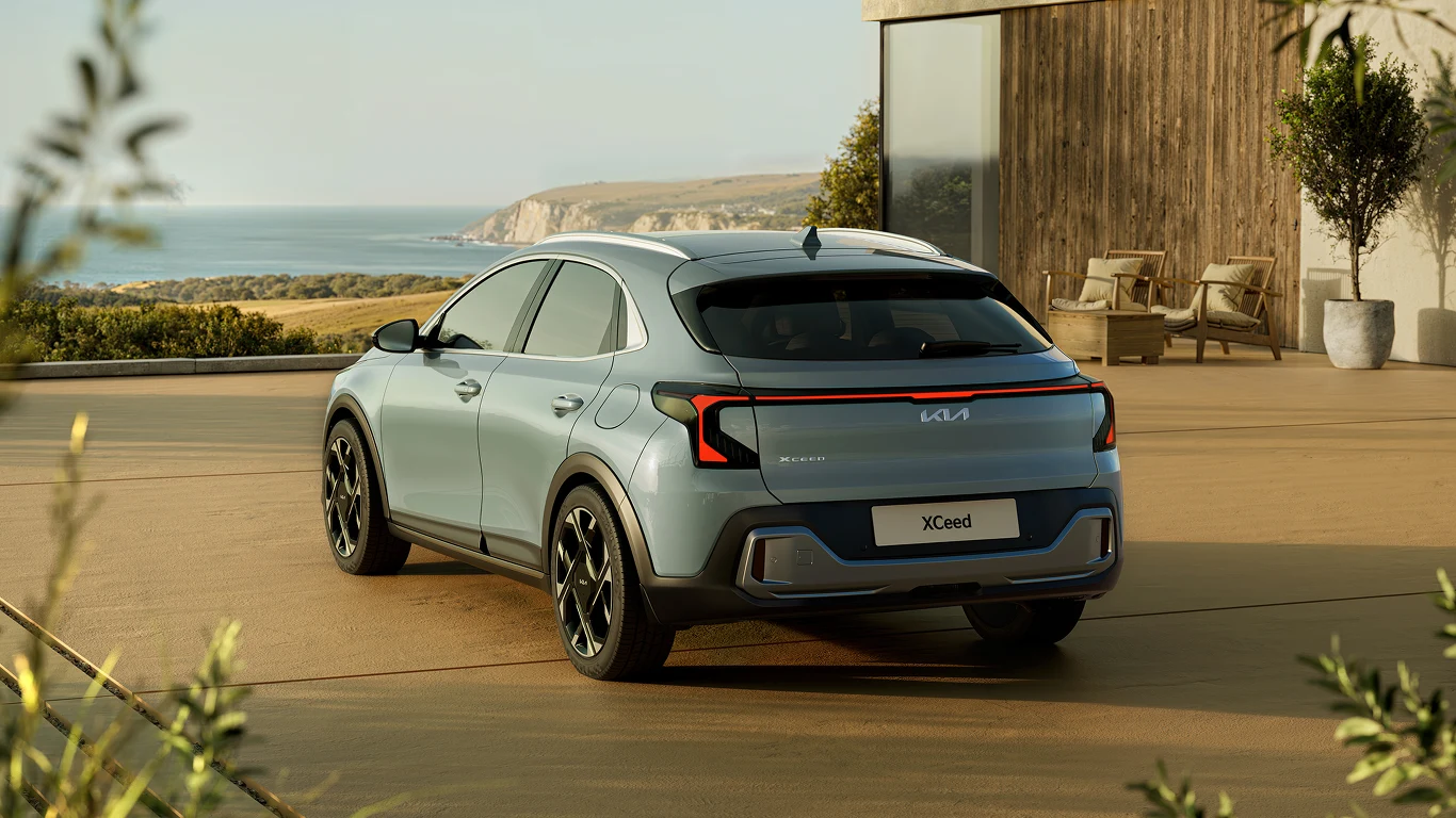 Srebrny crossover Kia XCeed zaparkowany na tarasie z widokiem na klifowe wybrzeże i morze, obok nowoczesnego budynku z dużymi przeszkleniami.