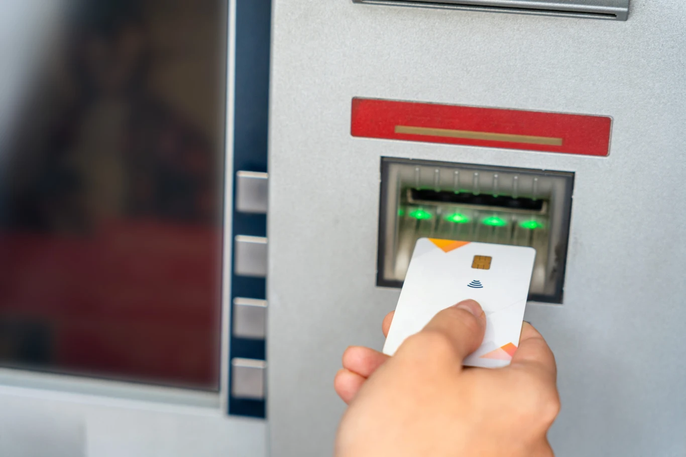 Ręka trzymająca kartę płatniczą w trakcie wkładania jej do bankomatu.