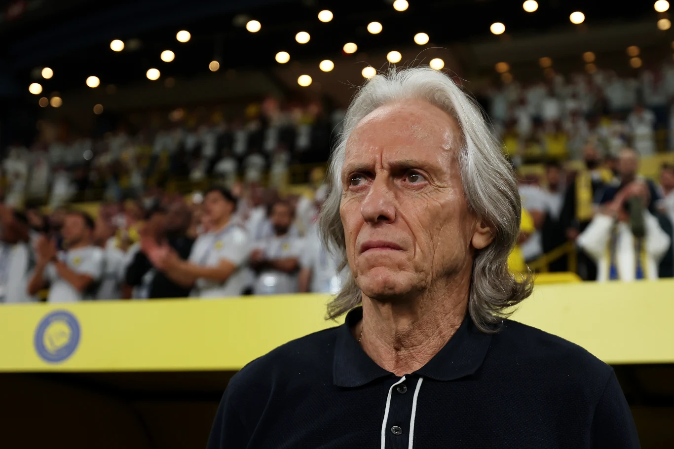 Jorge Jesus Mężczyzna o siwych włosach i poważnym wyrazie twarzy stoi na trybunach stadionu, w tle widoczny tłum kibiców.