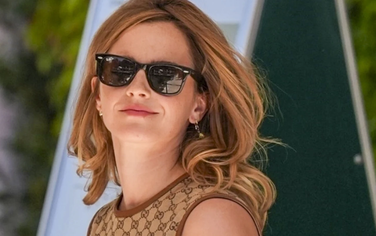Emma Watson Emma Watson w okularach przeciwsłonecznych i beżowej bluzce bez rękawów z brązowym wzorem, jasnobrązowe włosy.