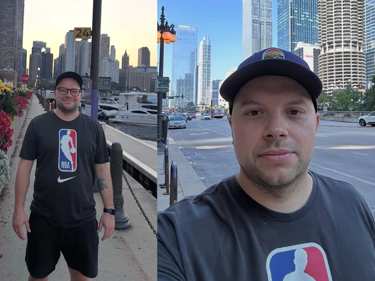 Mężczyzna w czapce z daszkiem i koszulce NBA stoi przy nabrzeżu oraz na tle nowoczesnych wieżowców w centrum miasta.