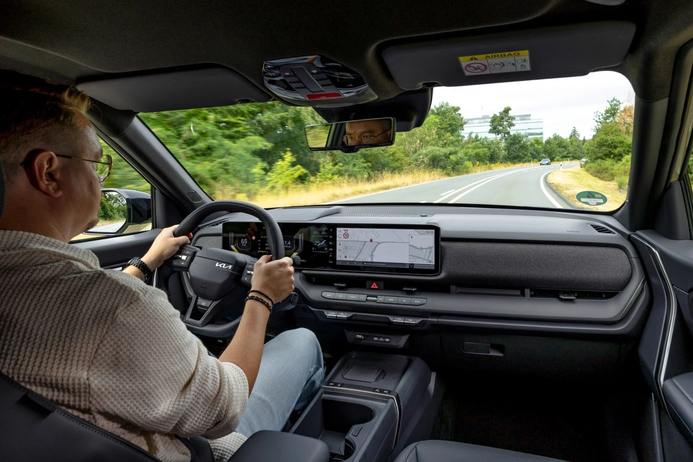 Mężczyzna prowadzący nowoczesny samochód SUV z cyfrowymi wyświetlaczami na desce rozdzielczej, jadący krętą drogą otoczoną zielenią.