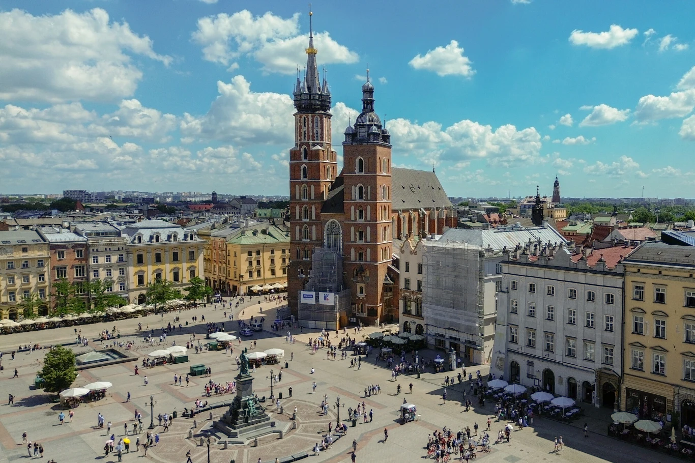 Bazylika Mariacka z charakterystycznymi dwiema wieżami dominuje nad Rynkiem Głównym w Krakowie, wokół którego gromadzą się liczni przechodnie i turyści, pośród zabytkowych kamienic i pomnika Adama Mickiewicza.
