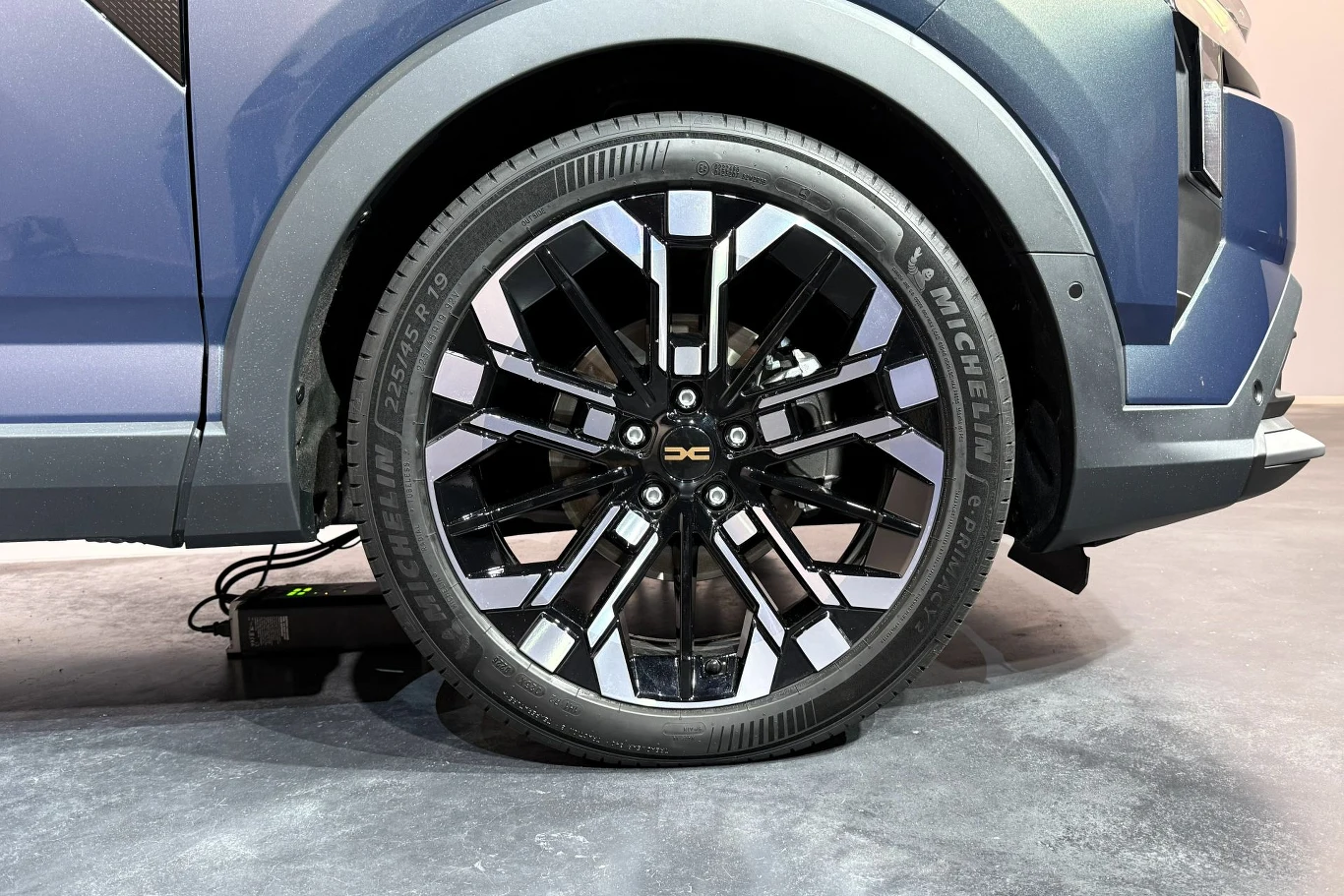 duże, czarne aluminiowe felgi z charakterystycznym wzorem oraz opona Michelin zamontowane w nowoczesnym nadkolu samochodu elektrycznego, z widocznym przewodem podłączonym do ładowania
